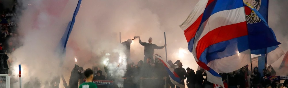 Leidenschaftliche Fans in einem französischen Stadion mit großen Fahnen und atmosphärischer Pyrotechnik während eines Ligue 1 Spiels.